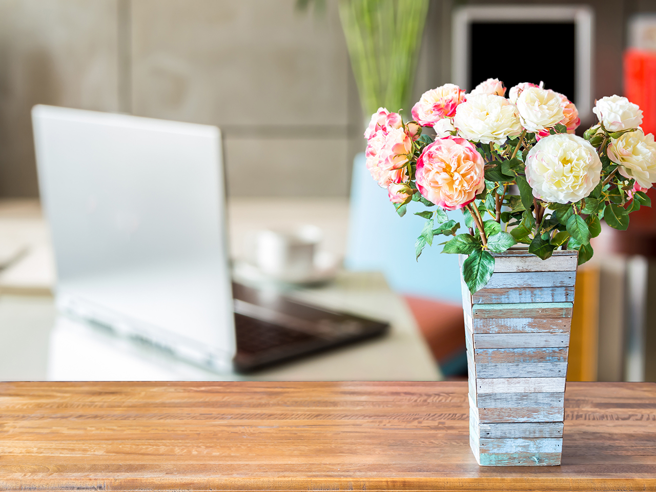 Artificial-flower-vase-over-blurred-image-of--modern-workspace-background